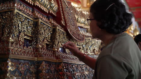 Skilled-artisan-working-to-repair-ornate-decoration-in-Thai-Buddhist-temple,-using-fine-tools-and-gold-paintwork
