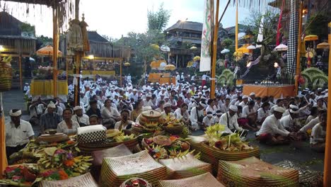 Balinese-People-Pray-in-Crowds-in-Hindu-Temple-Ceremony-at-Dusk,-Colorful-Coconut-Offerings-and-Flowers-around-Samuan-Tiga-Bedulu