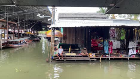 Clothes-and-souvenir-vendors-sat-beside-their-stalls-and-awaited-customers-in-Damnoen-Saduak-Floating-Market,-Ratchaburi-province,-South-West-of-Bangkok,-Thailand