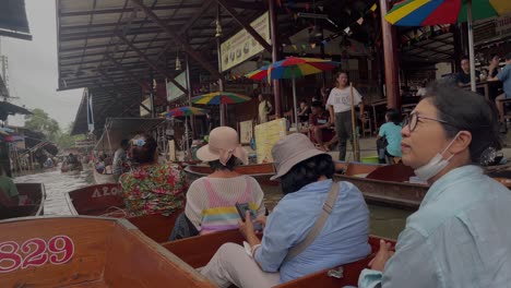 Tourists-take-selfies-and-enjoy-the-boat-ride-in-Damnoen-Saduak-Floating-Market,-the-vibrant-atmosphere-and-colourful-scenery-in-Ratchaburi-province,-South-West-of-Bangkok,-Thailand