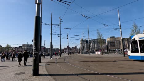Vista-De-Las-Líneas-Eléctricas-Del-Tranvía-Fuera-De-La-Estación-Central-De-Amsterdam-Con-Gente-Caminando