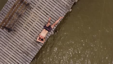An-orbital-aerial-shot-of-a-man-lying-down-on-the-wooden-jetty-at-the-Parana-River-in-Argentina