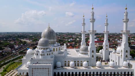 Luftaufnahme-Einer-Großen-Weißen-Moschee-Mit-Kuppel-Und-Minaretten-Vor-Bewölktem-Blauem-Himmel