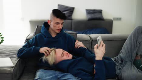 Happy-men-homosexual-couple-sit-on-sofa-and-using-smartphone,-talking