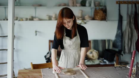Red-haired-potter-girl-works-with-a-piece-of-clay-using-a-rolling-pin