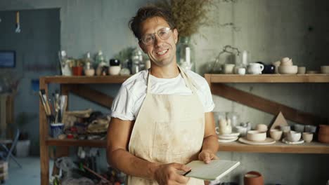 Portrait-of-a-young-happy-potter-posing-in-his-pottery-studio