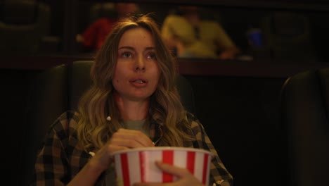 Woman-sitting-in-armchair-watching-a-horror-movie-at-the-cinema,-scatters-the-popcorn-from-fear
