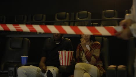 African-American-young-couple-came-to-the-movie-theatre-watching-film-while-a-man-in-a-protection-costume-stretching-warning