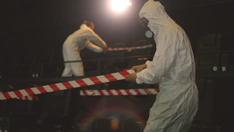 Quarantine-due-to-coronavirus-pandemia---two-men-in-protection-costume-stretching-warning-ribbons-over-seats