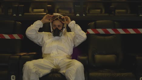 Portrait-of-a-man-in-white-protection-costume-and-respirator-sitting-alone-at-the-cinema-then-remove-it