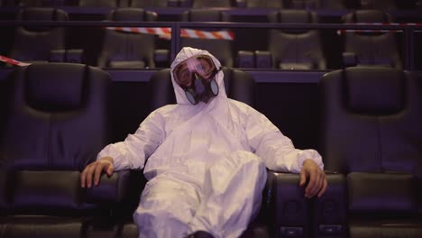 A-man-in-white-protection-costume-and-respirator-sitting-alone-at-the-cinema