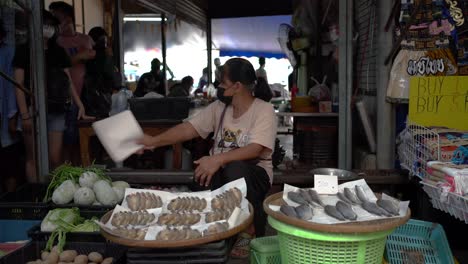 Vendors-sell-fish-and-await-customers-in-Maeklong-Railway-Market,-a-unique-and-fascinating-attraction-in-Samut-Songkhram-province,-Southwest-Bangkok,-Thailand