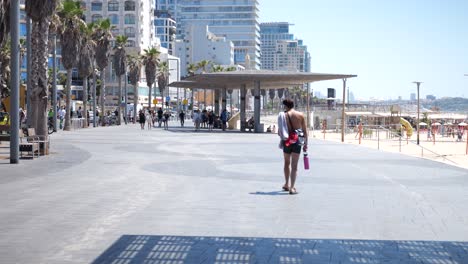 Shot-of-a-man-walking-in-the-city-of-Tel-Aviv-shirtless-and-carrying-a-drink-bottle