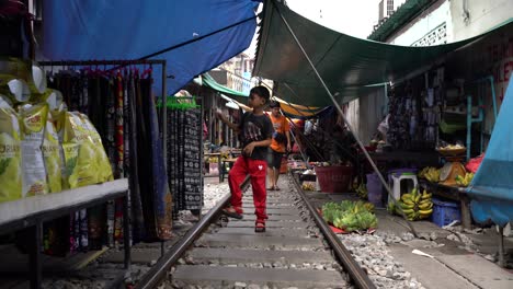 People-walk-on-the-railway-track-in-Maeklong-Railway-Market,-known-as-the-"umbrella-pulldown"-market,-a-unique-and-fascinating-attraction-in-Samut-Songkhram-province,-Southwest-Bangkok,-Thailand