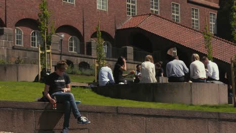 People-sit-on-a-wall-near-a-building-as-they-talk-and-eat-lunch