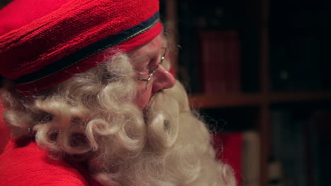 Santa-Claus-is-viewed-in-profile-from-the-right-side-during-an-interview-as-he-appears-to-reluctantly-agree-with-a-statement-from-the-interviewer,-filmed-in-slow-motion