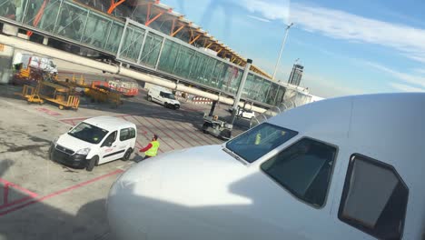 Airport-facilities-service-person-entering-a-small-car-on-tarmac-while-passengers-are-boarding-an-airplane-using-a-boarding-bridge,-air-bridge,-in-background