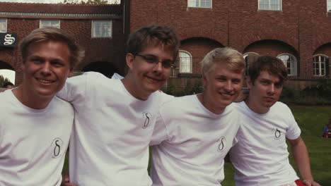 Four-friends-in-matching-white-shirts-sit-close-together-smiling-and-laughing