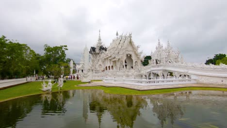 Pan-shot-of-a-pond-and-the-white-temple-in-Chiang-Rai,-on-a-cloudy-day,-in-Thailand,-Asia
