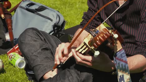 A-nyckelharpa,-also-referred-to-as-a-key-or-keyed-fiddle-and-sometimes-a-Swedish-violin,-played-outdoors-by-a-person-sitting-on-the-grass