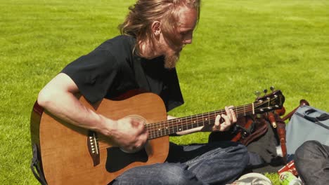 A-young-man-wearing-jeans-and-a-black-shirt-playing-acoustic-guitar-while-sitting-outside-on-the-grass