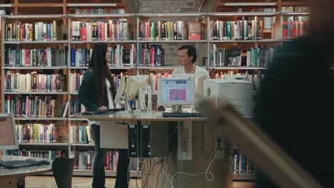 Wide-view-of-young-man-and-woman-having-a-conversation-in-the-library-while-standing-at-a-round-computer-table