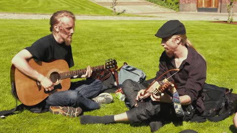 Two-men-play-acoustical-music-instruments-seated-outside-in-the-grass-on-a-sunny-day