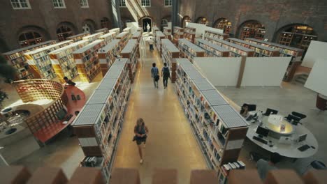 High-angle-view-looking-down-at-the-floor-of-the-university-library-and-the-symmetrical-rows-of-bookshelves-as-students-study-and-walk-through-the-aisles