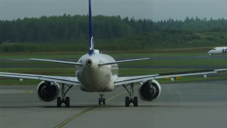 Close-up-of-an-airplane-leaving-the-gates-for-the-runway-while-a-small-aircraft-takes-off-in-the-background