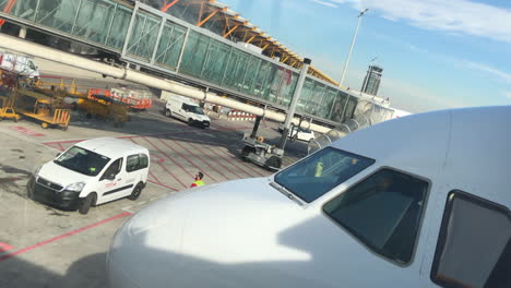 Airport-facilities-service-person-entering-a-small-car-on-tarmac-while-passengers-are-boarding-an-airplane-using-a-boarding-bridge,-air-bridge,-in-background