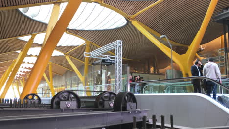 Modern-airport-terminal-with-people-using-escalators,-contemporary-architectural-design-combining-steel-and-wood-with-large-translucent-windows-in-the-ceiling,-travel,-transportation-and-architecture