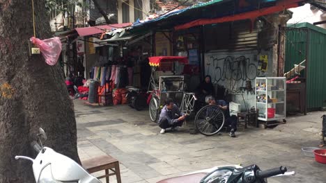 Men-working-and-fixing-cart-wheel-on-the-sidewalk-in-Hanoi,-Vietnam