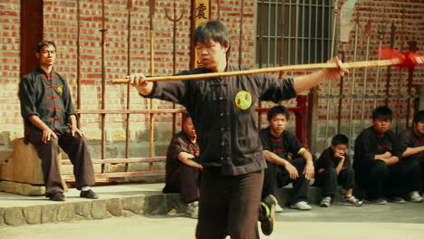 Martial-Arts-School-Students-watching-Young-Man-practicing-with-Spear