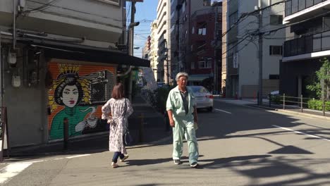 People-wakling-down-the-streeti-n-Osaka,-Japan-in-front-of-grafitti-wall