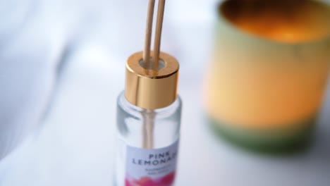 Close-up-of-a-reed-diffuser-bottle-with-wooden-sticks-and-a-scented-candle-in-the-background