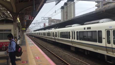 Main-waiting-at-train-station-in-Osaka,-Japan-with-a-train-coming-behind-him