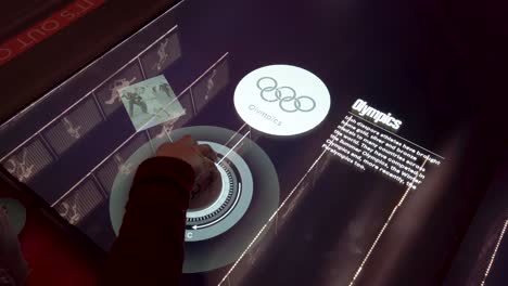 Pov-shot-of-a-hand-operating-a-wheel-mouse-and-using-an-interactive-video-display-showing-famous-moments-of-Irish-sportsmen-in-the-Olymic-Games-on-a-screen-in-EPIC---The-Irish-Emigration-Museum