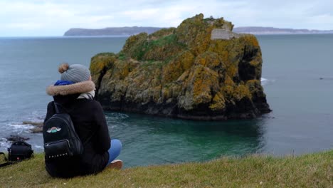 Person-sitting-on-Ireland-coastal-cliff-observing-rocky-coast-shoreline-formation-ocean-island