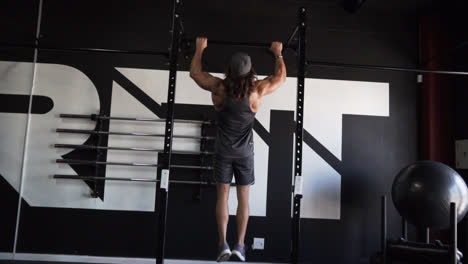 Muscular-man-with-long-hair-doing-pull-ups-in-a-dark-gym-with-camera-movement