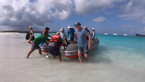 Boat-operators-are-holding-a-boat-white-tourists-are-disembarking-on-a-white-sand-beach-of-the-Galapagos-Islands