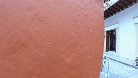 An-orange-wall-of-a-street-of-the-old-town-of-Cartagena-de-Indias,-Colombia,-where-several-palenqueras-and-tourists-are-standing-and-walking-on-the-street-and-sidewalk