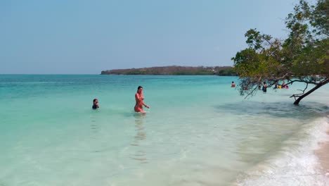 A-woman-and-her-son-are-walking-out-towards-the-shore-on-a-paradisiac-beach-with-clear,-transparent-and-turquoise-ocean-water