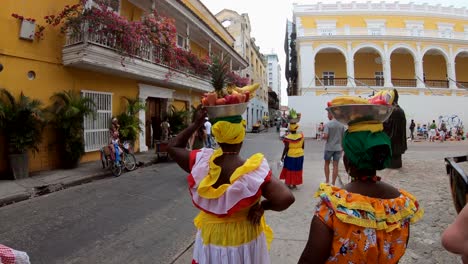 Palenqueras-Gekleidet-Mit-Bunten-Kleidern-Und-Balancierenden-Obstschalen-Im-Kopf-In-Der-Altstadt-Von-Cartagena-De-Indias,-Kolumbien