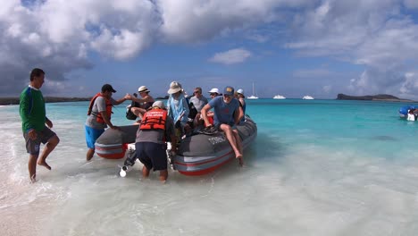 A-male-tourist-is-trying-to-disembark-on-a-white-sand-beach-and-clear-water-ocean-of-the-Galapagos-Islands-while-people-hold-the-boat