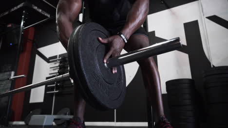 Black-muscular-man-placing-heavy-weights-on-to-a-weight-bar-in-a-dark-gym