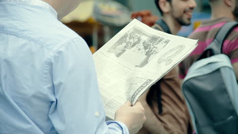 Man-Reading-Newspaper-Article-Standing-in-Public,-Urban-Scene