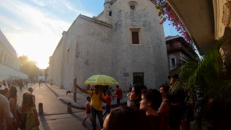 A-guide-with-a-yellow-umbrella-is-guiding-a-group-of-tourists-through-the-old-town-of-Cartagena-de-Indias,-Colombia-during-sunset