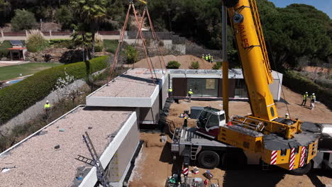 Heavy-crane-placing-rooftop-panel-of-modular-house,-aerial-view