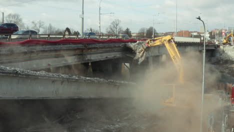 Excavator-demolishing-concrete-highway-bridge,-part-collapses-in-dust