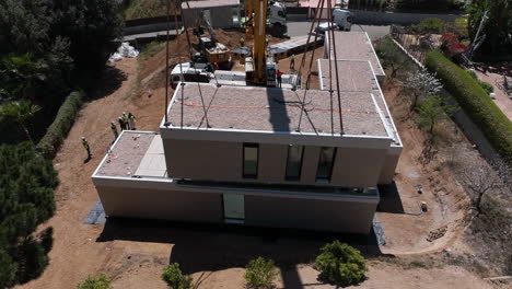 Industrial-crane-placing-modular-home-block-into-place,-aerial-drone-view
